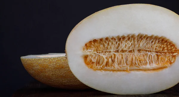 A ripe melon cut in half with seeds on a black background.