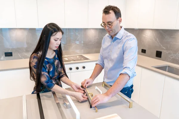 Male interior designer with female customer holding kitchen cabinet handles in configuration to make a selection for their home interior decor.
