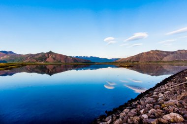 Dağlar, İzlanda 'daki Snaefellsnes Yarımadası' ndaki bir yolun geçtiği lav tarlalarının etrafındaki durgun sulara yansıyor.