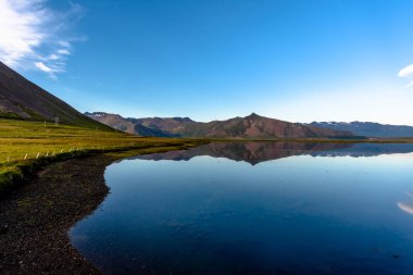 Dağlar, İzlanda 'daki Snaefellsnes Yarımadası' ndaki bir yolun geçtiği lav tarlalarının etrafındaki durgun sulara yansıyor.