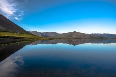 Dağlar, İzlanda 'daki Snaefellsnes Yarımadası' ndaki bir yolun geçtiği lav tarlalarının etrafındaki durgun sulara yansıyor.