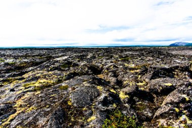 İzlanda 'nın Nordurping belediyesinde Husavik yakınlarındaki Mivatn Gölü' nde bulutlu mavi gökyüzü olan kumda lav kayaları var.