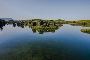 Yansımaları ve adaları olan volkanik Myvatn Gölü, Kuzey İzlanda 'da yeşil çayırlar ve mavi gökyüzü