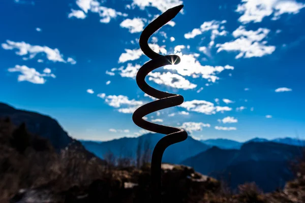 backlight of a rusty iron spiral from time on the blue sky and mountains background