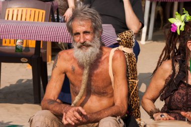 An unidentified older man with a beard sits at the annual festival of Freaks, Arambol beach, Goa, India clipart