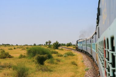 Indian train driving through across the plain. clipart