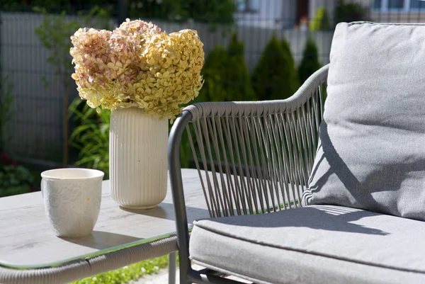 ceramic mug, vase with hydrangea flowers and comfortable armchair on terrace