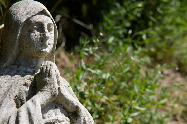 ancient stone figure of praying Holy Mary at cemetery