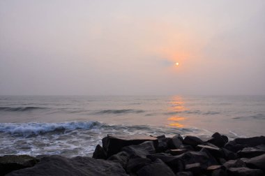 Rising sun overlooking the ocean and stone shore in Pondicherry, Tamil Nadu, India clipart