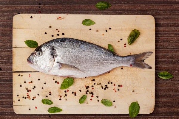 Fish on wooden board with herbs and spices. — Stock Photo, Image