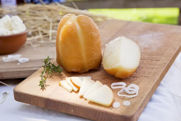 Uzené plátky sýra a velký kus na dřevěné desce. — Stock fotografie