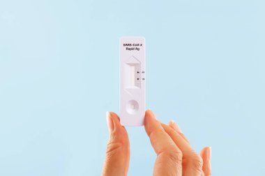 Mavi arka planda COVID-19 koronavirüs antijen testi yapan bir kadın. Evde kendini sınama.