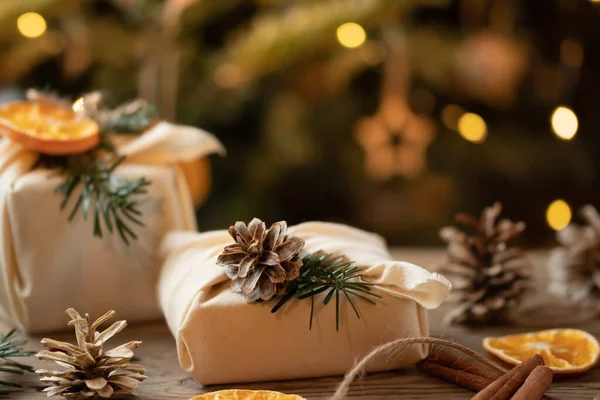 Concept de Noël zéro déchet. Emballé dans des cadeaux en tissu naturel et des décorations à partir de matériaux naturels sur une table en bois près de l'arbre de Noël avec des lumières — Photo