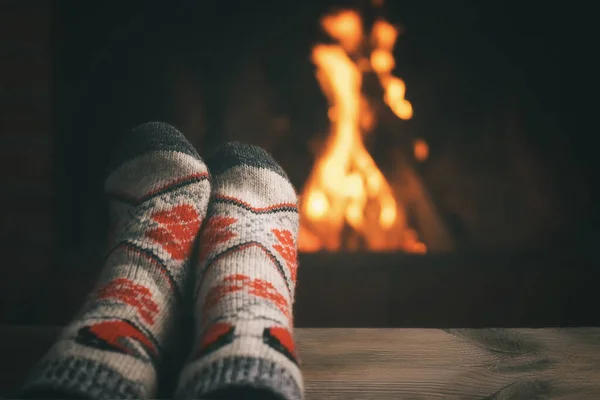 Lány pihen és melegíti a lábát egy égő kandalló egy vidéki házban egy téli estén. Szelektív fókusz — Stock Fotó
