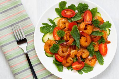 Beyaz bir tabakta taze karides, domates, roka ve otlardan oluşan salata.