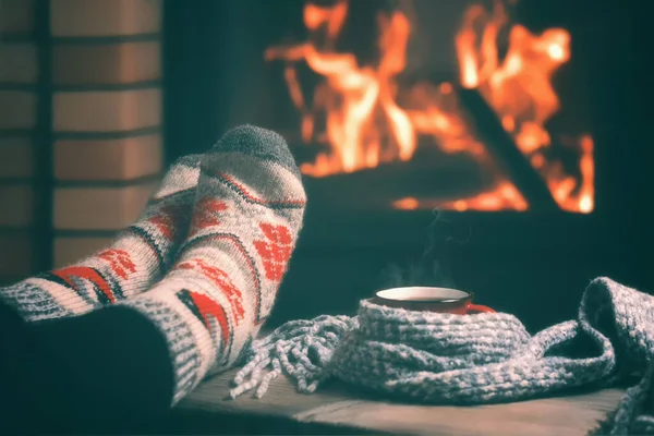 Mädchen, das an einem Winterabend an einem brennenden Kamin in einem Landhaus ruht und sich die Füße wärmt. Selektiver Fokus. — Stockfoto