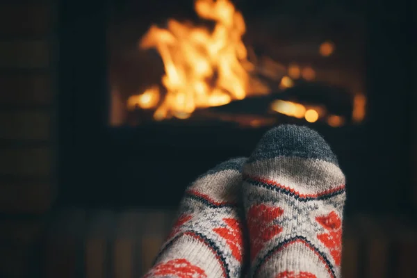 Mädchen, das an einem Winterabend an einem brennenden Kamin in einem Landhaus ruht und sich die Füße wärmt. Selektiver Fokus. — Stockfoto