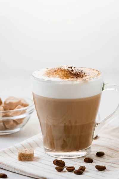 Café con leche vertido en capas con espuma y una tapa de chocolate crujiente en una mesa de cocina ligera. Imagen vertical con espacio de copia — Foto de Stock