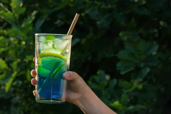 Hohe Gläser mit einem blauen Lagunencocktail in weiblicher Hand vor der grünen Kulisse im Hof. Selektiver Fokus — Stockfoto