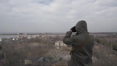 Gaz maskeli bir adam çatıdan boş bir alanı inceliyor. Kıyamet sonrası ortam.
