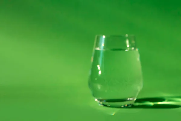 Blurred glass of clean fresh water on green background. Spring ecologically pure water. Detox, energy of still water. out of focused. Absinthe or alcohol through the eyes of a drunkard
