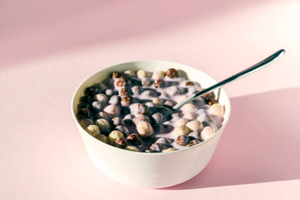 Bowl of chocolate vanilla breakfast with cereal balls, milk or yogurt on pink background. Healthy dry crispy corn balls
