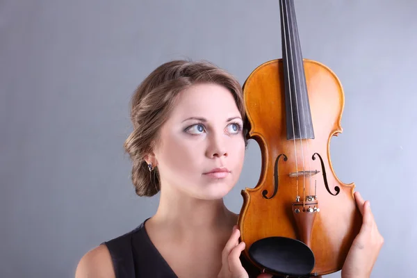 Krásná a jemná dívka drží housle na šedém pozadí — Stock fotografie