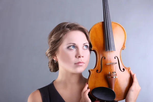 Beautiful and gentle girl is holding a violin on a gray background — Stock Photo, Image