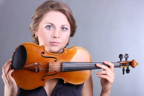 Menina bonita e gentil está segurando um violino em um fundo cinza — Fotografia de Stock