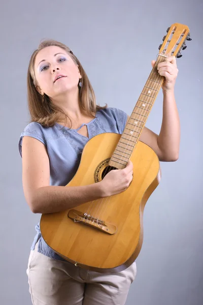 Vacker flicka med blå ögon spela gitarr på grå bakgrund — Stockfoto