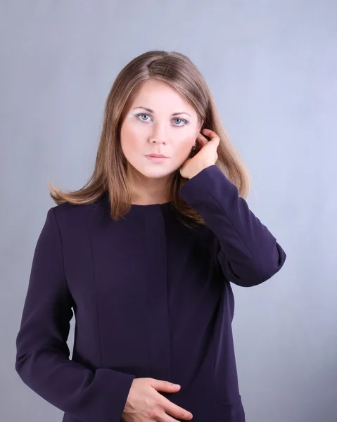 Vacker flicka i en blå jacka och en lång aftonklänning på en grå bakgrund — Stockfoto