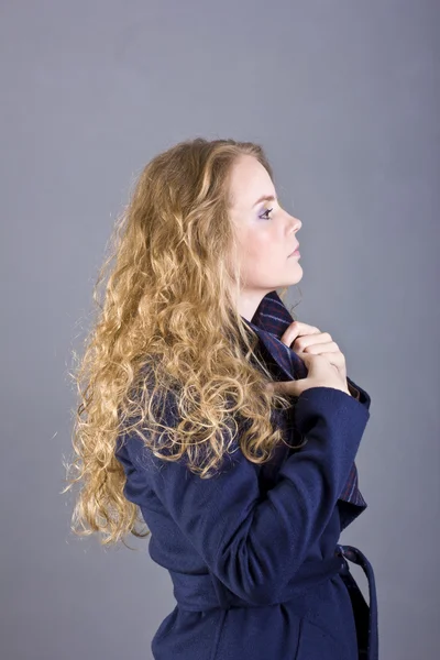 Prachtige krullende blonde met een lome gezicht in de blauwe vacht op grijze achtergrond — Stockfoto