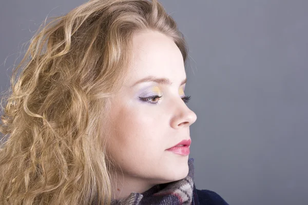 Schöne lockige Blondine mit schwachem Anblick im blauen Mantel auf grauem Hintergrund — Stockfoto