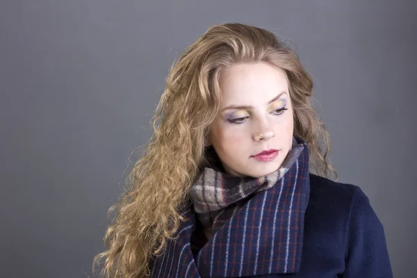Beautiful curly blonde with a languid sight in the blue coat on gray background — Stock Photo, Image