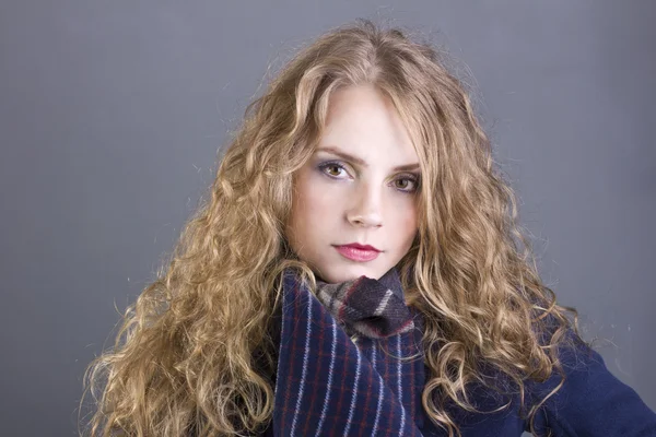 Bella bionda riccia con una vista languida nel cappotto blu su sfondo grigio Foto Stock