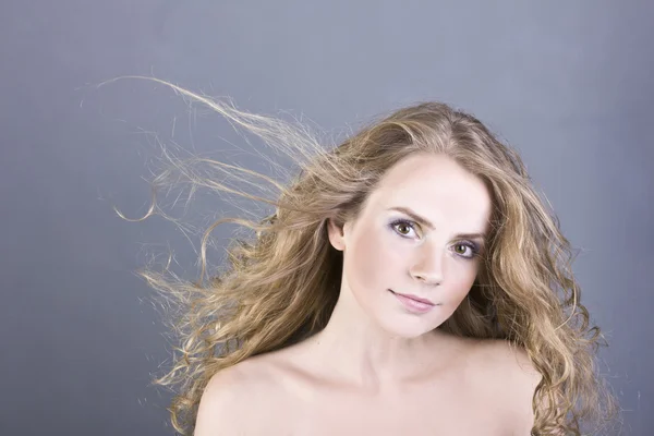 The beautiful blonde with long curly hair and brown eyes on a gray background — Stock Photo, Image