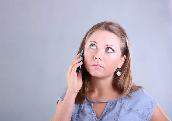 Hermosa joven con ojos azules habla por teléfono móvil sobre un fondo gris — Foto de Stock