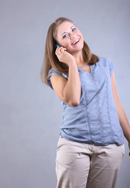 Schönes junges Mädchen mit blauen Augen spricht per Handy auf grauem Hintergrund — Stockfoto