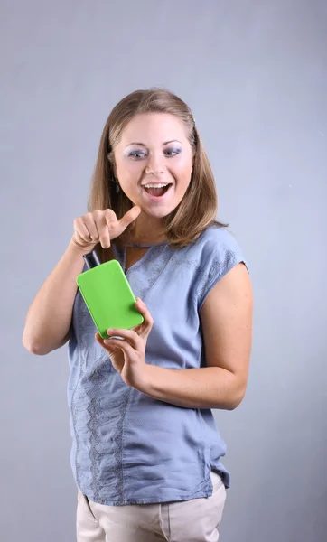 Hermosa joven feliz chica con ojos azules sosteniendo una botella verde brillante sobre un fondo gris — Foto de Stock