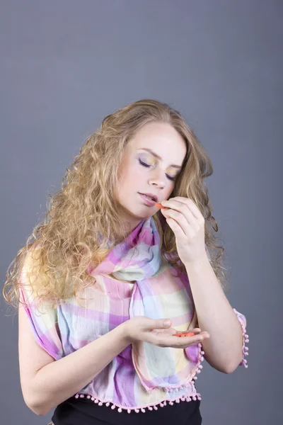 Hermosa chica con pelo rizado blanco sosteniendo pastillas sobre un fondo gris — Foto de Stock