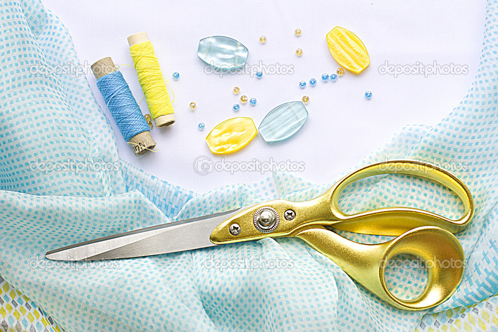Large scissors with gold handles lie on a beautiful yellow-blue silk cloth