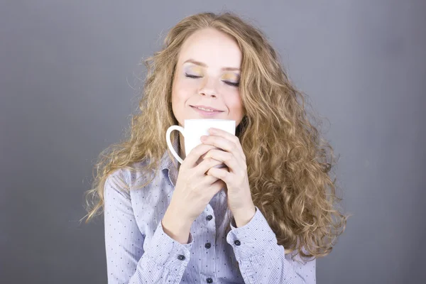 Härlig blondin med lockigt hår dricker te eller kaffe från en vit mugg — Stockfoto