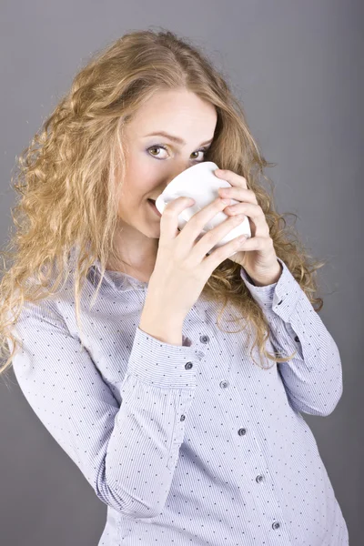 Härlig blondin med lockigt hår dricker te eller kaffe från en vit mugg — Stockfoto
