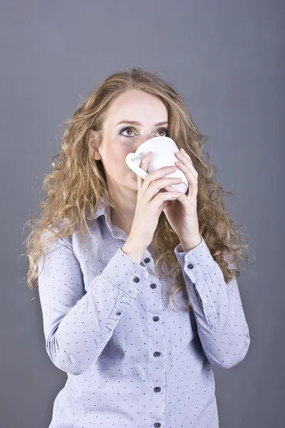 Härlig blondin med lockigt hår dricker te eller kaffe från en vit mugg — Stockfoto