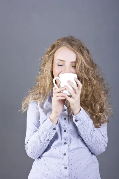 Härlig blondin med lockigt hår dricker te eller kaffe från en vit mugg — Stockfoto