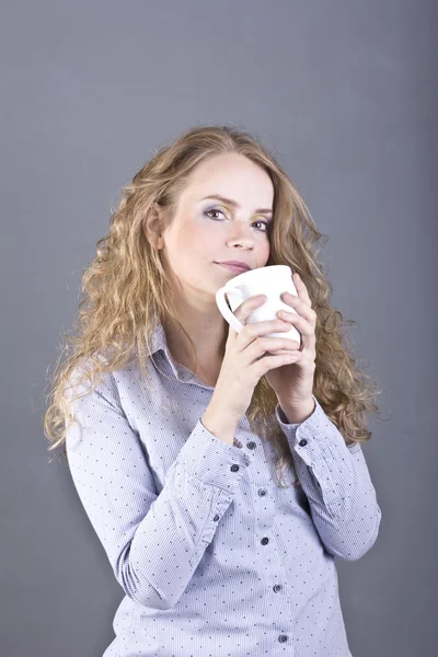 Härlig blondin med lockigt hår dricker te eller kaffe från en vit mugg — Stockfoto