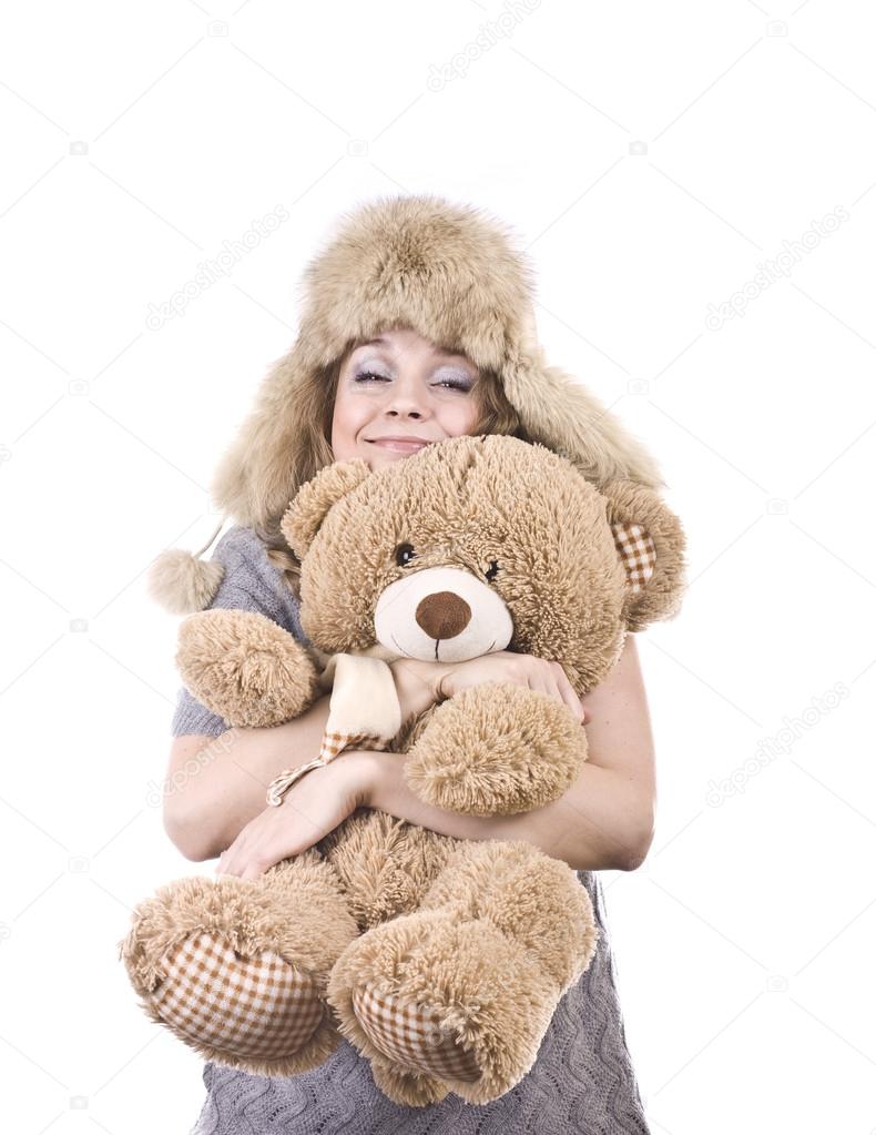 Cute blonde in fur hat with a large teddy bear in her arms on a white background