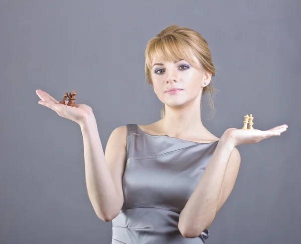 Schönes junges Mädchen mit Schachfiguren in der Hand auf grauem Hintergrund — Stockfoto