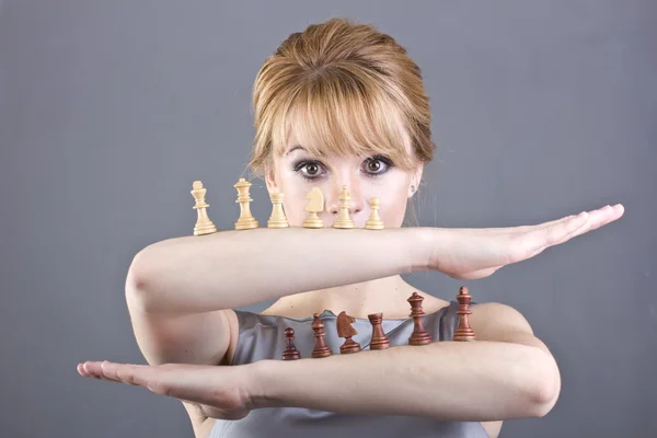 Vacker ung flicka med schackpjäser i handen på grå bakgrund — Stockfoto