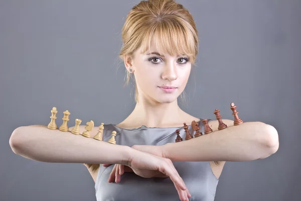 Menina bonita segurando peças de xadrez na mão sobre fundo cinza — Fotografia de Stock
